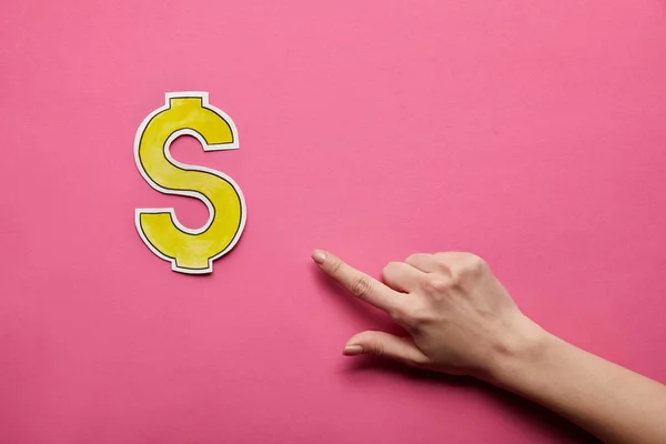 Vista superior del dedo apuntando al signo del dólar sobre fondo rosa - foto de stock
