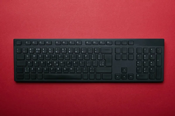 Vue du dessus du clavier d'ordinateur en plastique noir sur fond rouge — Photo de stock