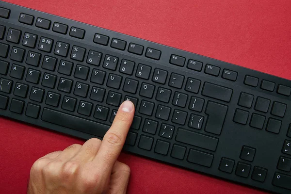 Vista recortada del hombre pulsando el botón en el teclado del ordenador negro sobre fondo rojo - foto de stock