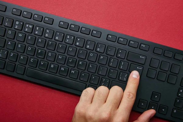 Vista superior del hombre pulsando el botón en el teclado del ordenador negro sobre fondo rojo - foto de stock