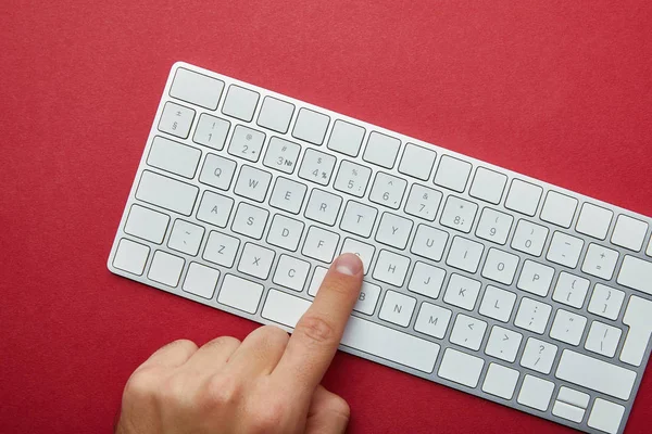 Vista recortada del hombre pulsando el botón en el teclado del ordenador blanco sobre fondo rojo - foto de stock