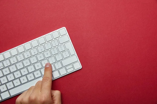 Cropped view of man pushing button on white computer keyboard on red background — Stock Photo