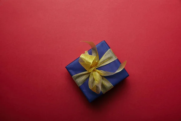 Vista superior del regalo envuelto con cinta dorada sobre fondo rojo — Stock Photo