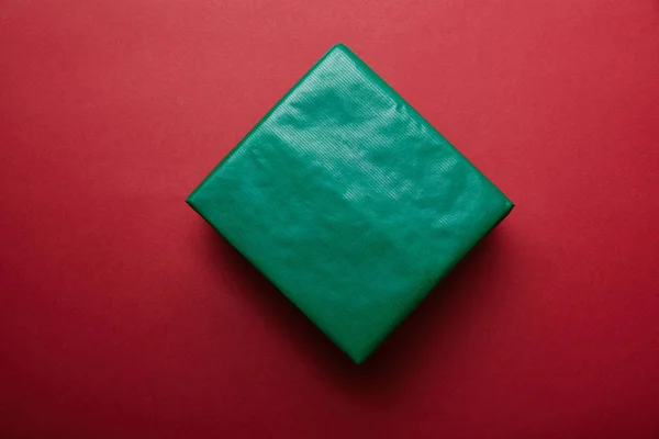 Top view of gift wrapped in green wrapping paper on red background — Stock Photo