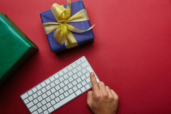 Vue du dessus du doigt de l'homme appuyant sur le bouton sur le clavier de l'ordinateur près de cadeaux colorés sur fond gris — Photo de stock