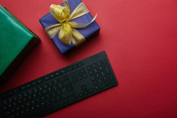 Cropped view of gifts near black computer keyboard on red background — Stock Photo