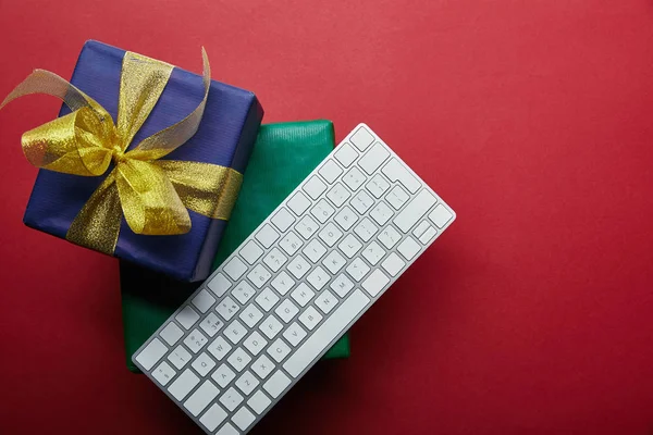 Вид сверху на роскошные подарки рядом с белой компьютерной клавиатурой на красном фоне — стоковое фото