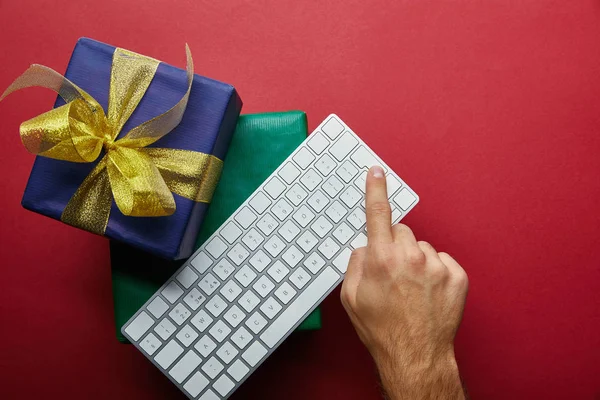 Vue du dessus de l'homme appuyant sur le bouton sur le clavier de l'ordinateur près de cadeaux sur fond rouge — Photo de stock