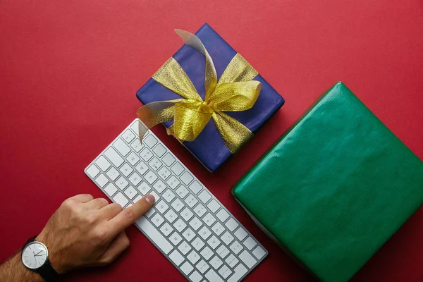 Vue du dessus du bouton-poussoir homme sur clavier d'ordinateur blanc près de cadeaux colorés sur fond rouge — Photo de stock