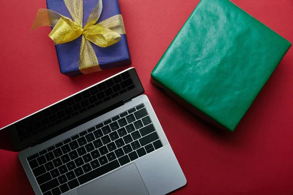 Vue recadrée de l'ordinateur portable avec clavier d'ordinateur portable près de cadeaux enveloppés sur fond rouge — Photo de stock