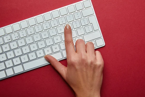 Вид зверху жінки натискає кнопку на білій клавіатурі комп'ютера на червоному тлі — стокове фото