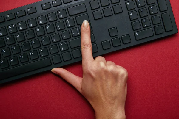 Vista superior de la mujer pulsando el botón en el teclado del ordenador negro sobre fondo rojo - foto de stock