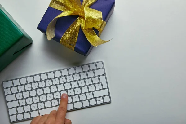 Обрізаний вигляд людини, що натискає кнопку на клавіатурі комп'ютера біля барвистих подарунків на сірому фоні — стокове фото