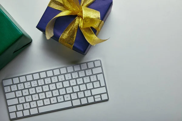 Vista recortada de regalos cerca del teclado de la computadora blanca sobre fondo gris - foto de stock