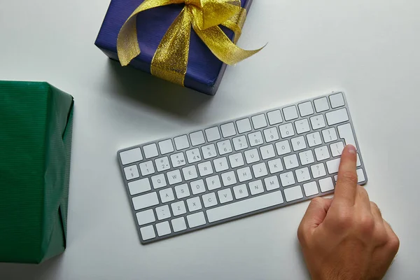 Top view of man pushing button on computer keyboard near wrapped boxes on grey background — Stock Photo