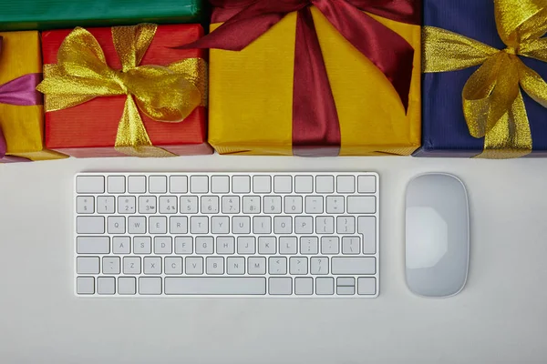 Vue du dessus des cadeaux près du clavier d'ordinateur et de la souris d'ordinateur sur fond blanc — Photo de stock