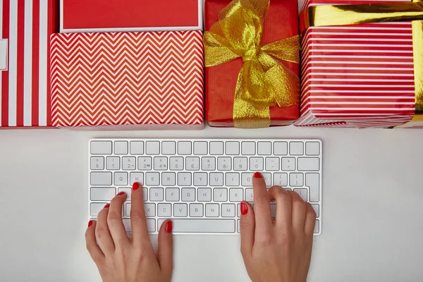 Vista superior de la mujer escribiendo en el teclado del ordenador blanco cerca de regalos de colores sobre fondo blanco - foto de stock