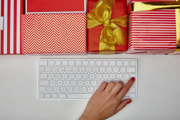 Vista superior de la mujer pulsando el botón en el teclado del ordenador cerca de regalos de colores sobre fondo blanco - foto de stock