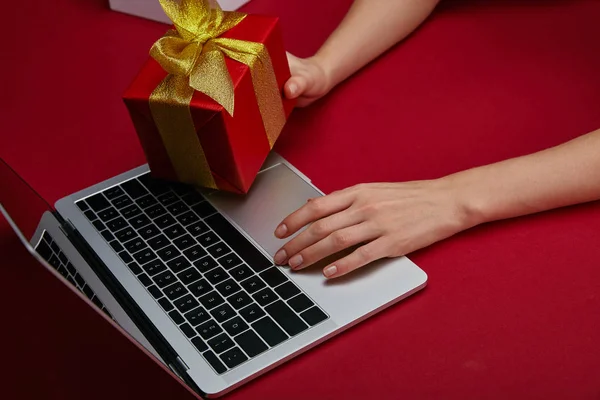 Cropped view of woman holding gift near laptop on red background — Stock Photo