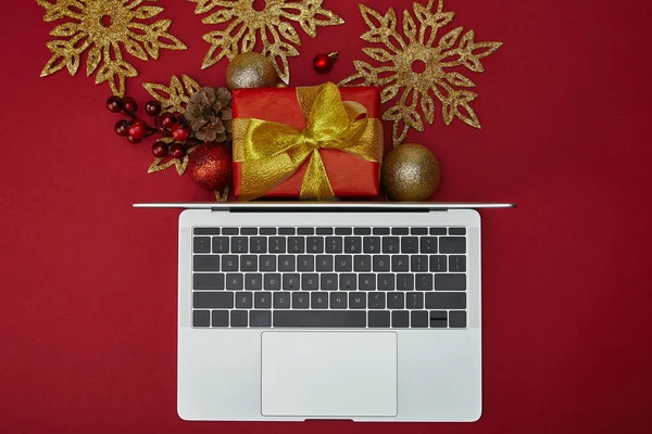 Vue du dessus de l'ordinateur portable près de cadeau enveloppé et décorations sur fond rouge — Photo de stock