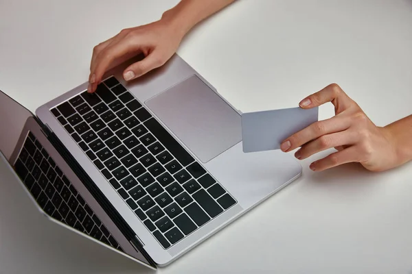 Vista recortada de la mujer que sostiene la tarjeta de crédito en la mano y el uso de ordenador portátil sobre fondo blanco - foto de stock