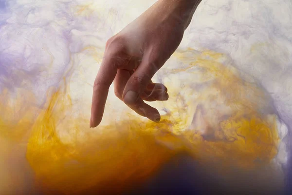 Vista parcial de la mano en agua con pintura naranja y púrpura - foto de stock