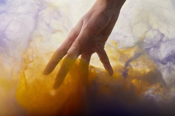 Vue recadrée de la main dans l'eau avec de la peinture orange et violet — Photo de stock