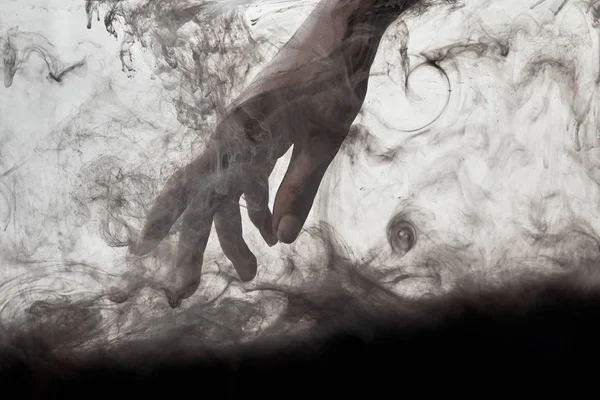 Женская рука в воде с вихрями черной краски — стоковое фото