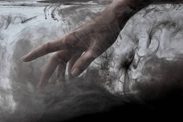 Vista recortada de la mano femenina en agua con pintura negra - foto de stock