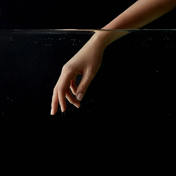 Partial view of girl putting hand into clear water isolated on black — Stock Photo