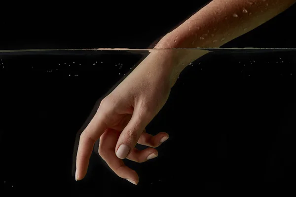 Woman putting hand into clear water isolated on black — Stock Photo