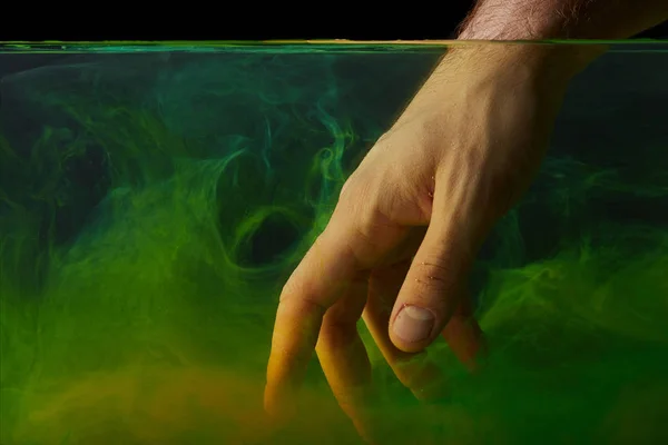 Partial view of male hand in water with green paint swirls — Stock Photo