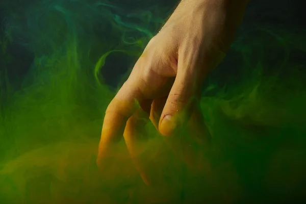Vista recortada de la mano en agua con remolinos de pintura verde - foto de stock