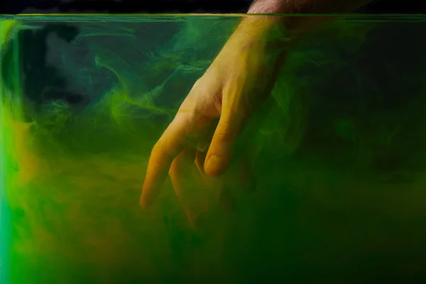 Cropped view of man putting hand into water with green paint — Stock Photo