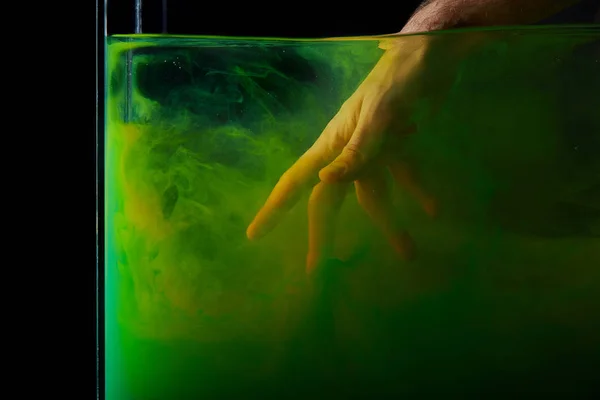 Mano masculina en agua con remolinos de pintura verde - foto de stock