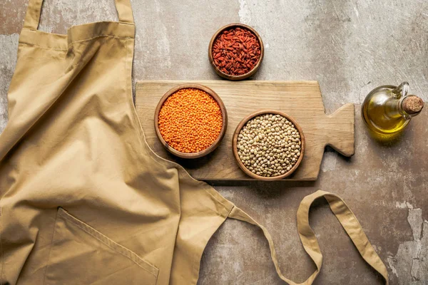 Flat lay of apron, legumes, goji berries on wooden board with rustic background — Stock Photo