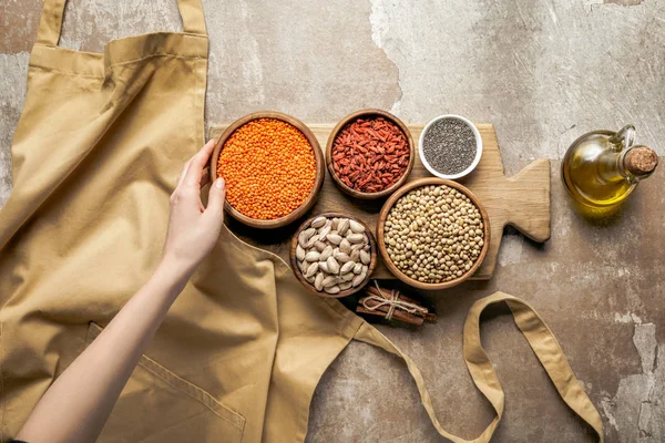 Cropped view of woman holding red lentils with goji berries and chia seeds on wooden board on rustic background — Stock Photo