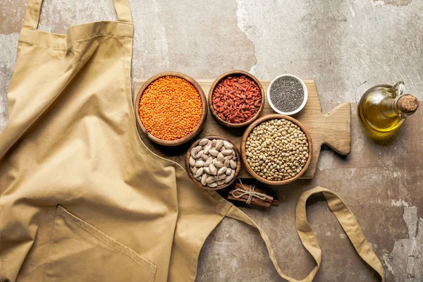 Flat lay of apron, legumes, goji berries and chia seeds on wooden board with rustic background — Stock Photo
