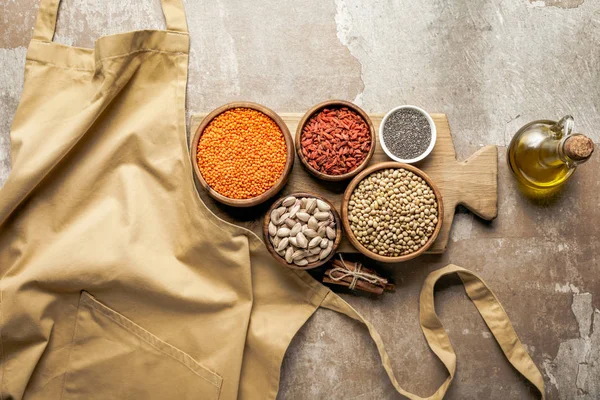 Colocação plana de avental, legumes, bagas de goji e sementes de chia em tábua de madeira com fundo rústico — Fotografia de Stock