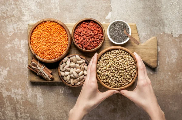 Vista recortada de la mujer sosteniendo soja con bayas de goji en tablero de madera con fondo rústico - foto de stock