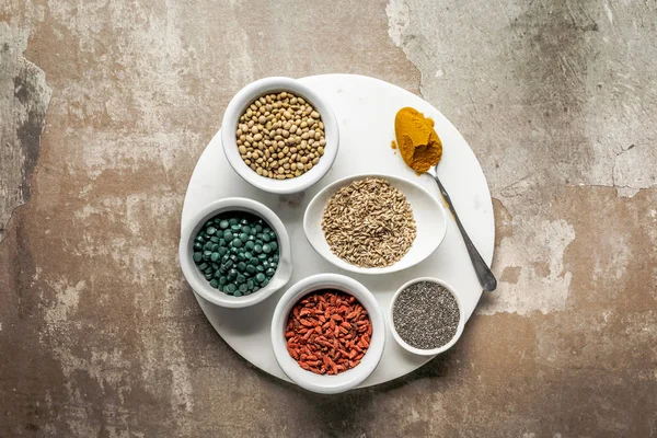 Vue de dessus des superaliments et des légumineuses sur plaque blanche avec fond rustique texturé — Photo de stock