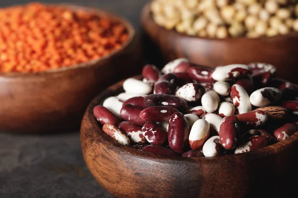 Close up of beans in wooden bowl with legumes on background — Stock Photo