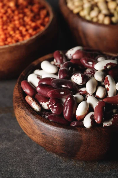 Close up of beans in wooden bowl with legumes on background — Stock Photo