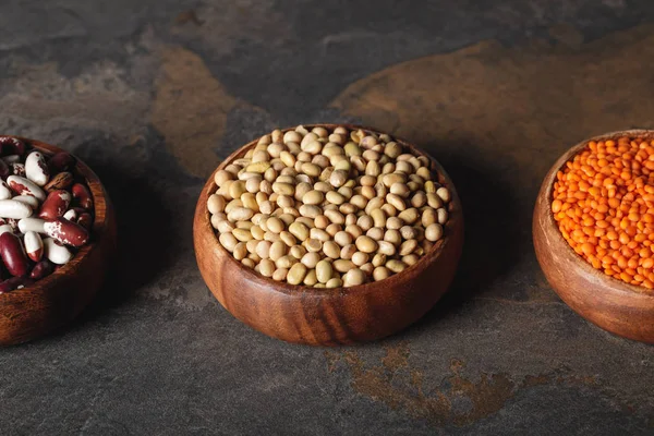 Frijoles, soja y lentejas en tazones de madera en la mesa - foto de stock