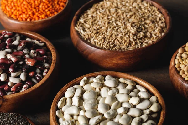 Assortment of beans, lentils and oat groats in wooden bowls on table — Stock Photo