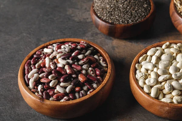 Variedade de feijões em tigelas de madeira com sementes de chia na mesa — Fotografia de Stock