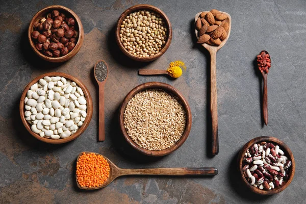 Flat lay of wooden bowls and spoons with superfoods, legumes and grains on table — Stock Photo