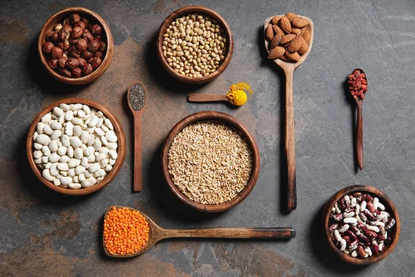 Tendido plano de cuencos de madera y cucharas con superalimentos, legumbres y granos en la mesa - foto de stock