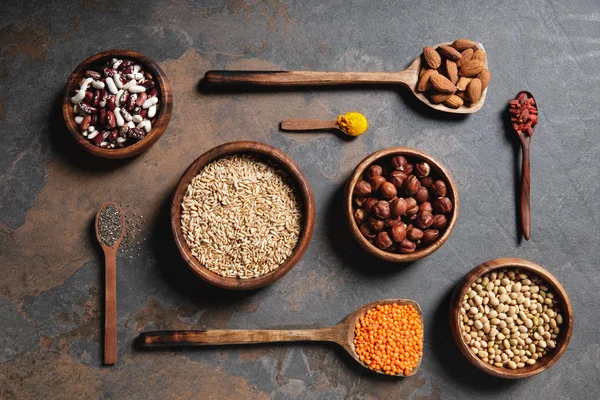 Vue de dessus des bols et cuillères en bois avec superaliments, légumineuses et grains sur la table — Photo de stock