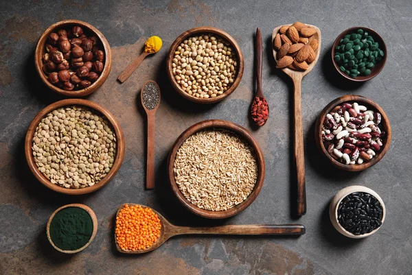 Flat lay of wooden bowls and spoons with superfoods, legumes and grains on table — Stock Photo